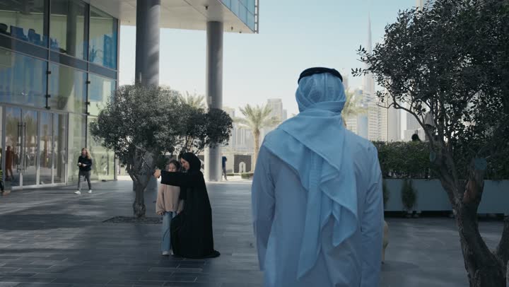 أم عربية خليجية إماراتية ترتدي الحجاب والعباءة تقوم بالتجول في الهواء الطلق برفقة ابنتها، التنزه في وقت العطلة في إحدى الاماكن العامة في الإمارات, امرأة سعودية تقوم بالتقاط صور السيلفي التذكارية باستخدام الهاتف المحمول بإيماءات السعادة والسرور