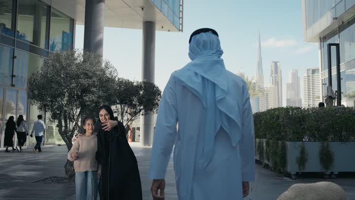 التنزه في وقت العطلة في إحدى الاماكن العامة في الإمارات, أم عربية خليجية إماراتية ترتدي الحجاب والعباءة تقوم بالتجول في الهواء الطلق برفقة ابنتها، امرأة سعودية تقوم بالتقاط صور السيلفي التذكارية باستخدام الهاتف المحمول بإيماءات السعادة والسرور