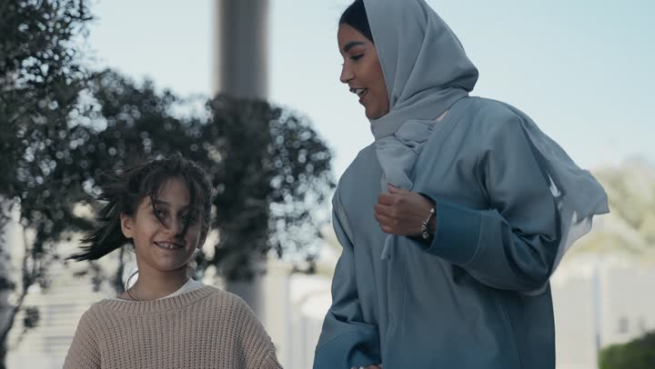 الاشارة إلى شيء ما، تبادل الأحاديث والأخبار بإيماءات السرور والفرح, عائلة سعودية تقوم بالتنزه في وقت العطلة في إحدى الاماكن العامة في الإمارات, تصوير مقرب لأم عربية خليجية إماراتية ترتدي الحجاب والعباءة تقوم بالمشي والتجول في الهواء الطلق برفقة ابنتها