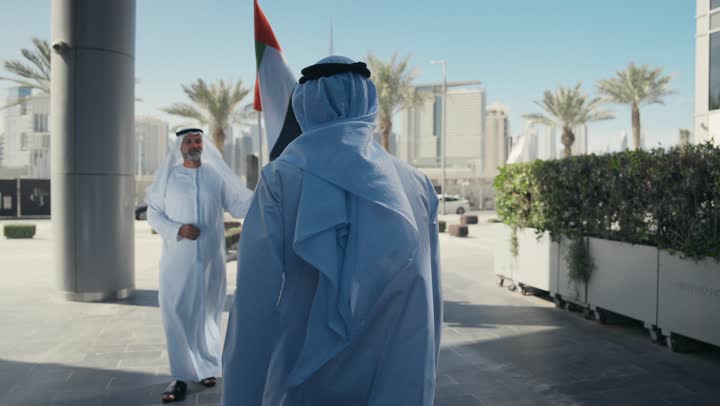 توارث حب الوطن والاعتزاز به، رفع راية البلاد للاعلى، الاحتفال بذكرى تأسيس الاتحاد 2 ديسمبر في الطريق، يوم العلم 3 نوفمبر، اليوم الوطني الاماراتي1971، رجل عربي خليجي اماراتي يرتدي الكندورة والغترة يقوم بتسليم علم الامارات العربية المتحدة لابنه بإيماءات الفخر