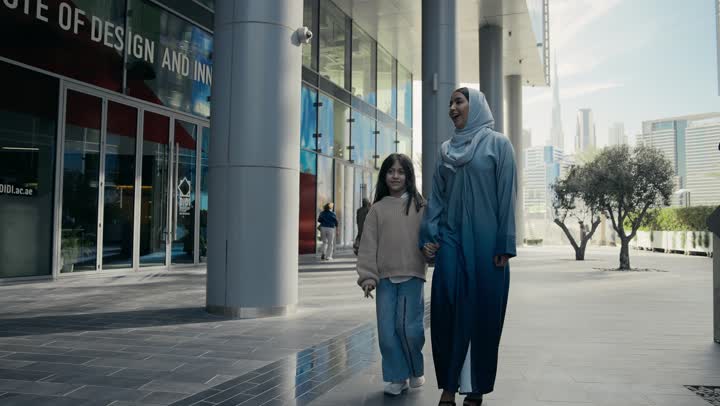 عائلة سعودية تقوم بالتنزه في وقت العطلة في إحدى الاماكن العامة في الإمارات, تبادل الأحاديث والأخبار بإيماءات السرور والفرح, أم عربية خليجية إماراتية ترتدي الحجاب والعباءة تقوم بالمشي والتجول في الهواء الطلق برفقة ابنتها، الاشارة إلى شيء ما، تقديم الاهتمام للأبناء
