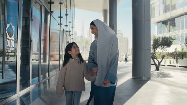A Saudi family is out for a walk during the holiday in a public place in the Emirates, exchanging conversations and news with gestures of pleasure and joy. An Emirati Gulf Arab mother wearing a hijab and abaya is walking and strolling in the open air with her daughter, pointing to something, giving attention to the children.