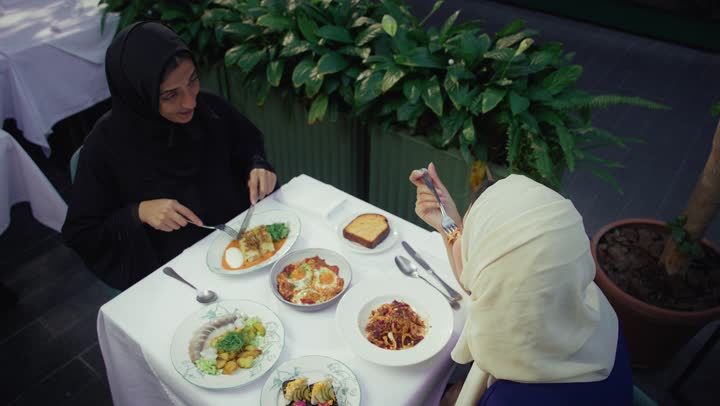 Having a good time, two Emirati Gulf Arab women sitting at a table in a cafe, developing social relations, chatting and having a good time with friends, an upscale coffee shop in the Emirates, expressions of happiness and pleasure at a gathering of friends, two Saudi friends exchanging talk.