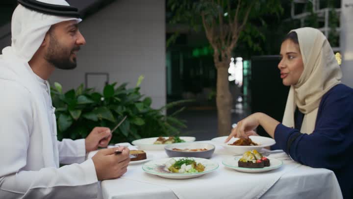 Gestures of pleasure and happiness, the concept of intimacy and love between family members, family dialogue and discussion, family entertainment activities and events, holiday entertainment, a close-up of an Emirati Gulf Arab man and his wife sitting in a cafe enjoying spending time outside.