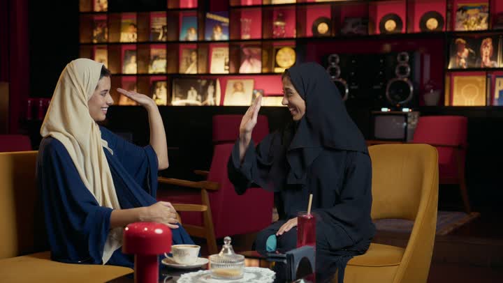 كوفي شوب راقي بالامارات، تعابير السعادة والسرور بلمة الرفاق، قضاء وقت ممتع مع الأصدقاء ، صديقتان سعوديتين تتبادلان الحديث ، تطوير العلاقات الإجتماعية، امرأتان عربيتين خليجيتين اماراتيتين تجلسان على طاولة في المقهى.
