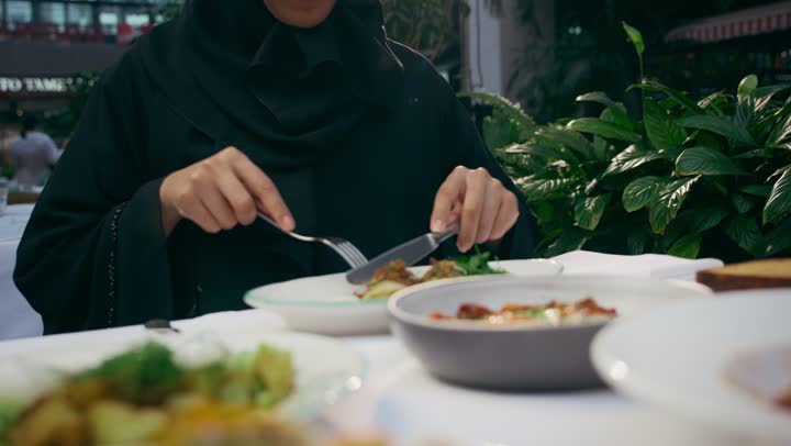 Gestures of happiness and pleasure, enjoying leisure activities, spending a pleasant time outside. Eating lunch at a restaurant, restaurants and cafes in the Emirates, a veiled Emirati Gulf Arab woman wearing casual clothes sitting at a table