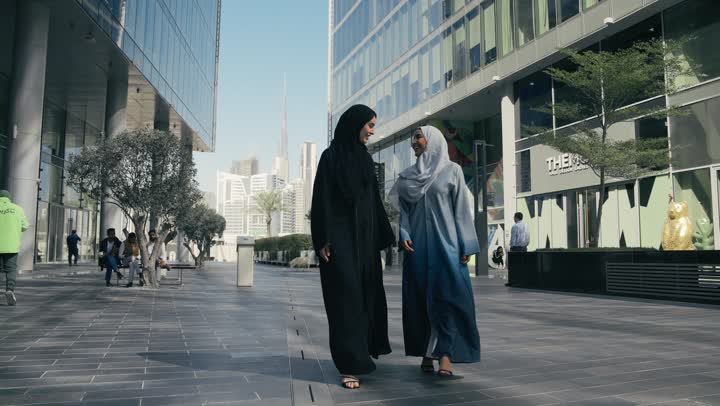 Two Saudi Arabian Gulf women talking about daily gossip, two smiling friends walking together on a pleasant outing to a recreational place, tourism and recreation, friendships and acquaintances, social relationships, spending a pleasant time