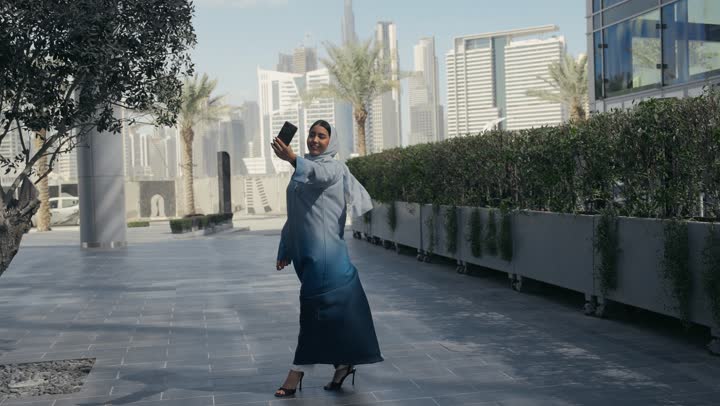 سيده اماراتيه انيقه ترتدي عباءه رماديه تلتقط صور تذكاريه عبر الهاتف المحمول، امرأه سعوديه تقوم بوثيق اللحظات السعيده، استخدام التقنيات الحديثه والمتطوره، التطور التكنولوجي