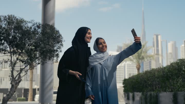 توثيق اللحظات السعيدة، استخدام الأجهزة والتقنيات المتطورة، امرأتان عربيتان خليجيتان محجبتان ترتديان العباءة الخليجيه تقومان بالتقاط صور سيلفي تذكارية بإيماءات السعادة والسرور، سيدتان سعوديتان تقومان بالتقاط صور تذكاريه