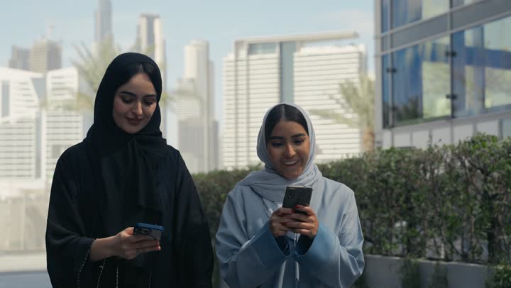 الاستعداد لالتقاط صورتذكارية عبرالجوال، النظر الى كاميره الموبايل بإيماءات السرور و السعادة،  سيدتان عربيتان سعوديتان خليجيتان ترتديان العباءة الخليجيه تقومان باخد صورة باستعمال الهاتف المحمول، امرأتان امراتيتان تقومان لالتقاط صور تذكارية عبرالهاتف