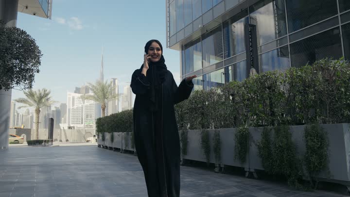Having a good time exchanging news and conversations with friends and family, a veiled Saudi Arabian Gulf woman wearing an abaya talking on a mobile phone, gestures of happiness and pleasure when making a phone call, an Emirati woman making a phone call with someone