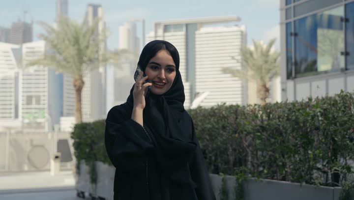 قضاء اوقات ممتعة بتبادل الاخبار والأحاديث مع الاصدقاء والأهل، إمرأة عربية سعودية خليجية محجبة ترتدي العباءة تقوم بالتحدث عبر الهاتف المحمول، ايماءات السعادة و السرور بإجراء مكالمة هاتفية، سيده اماراتيه تجري مكالمه هاتفيه مع شخص
