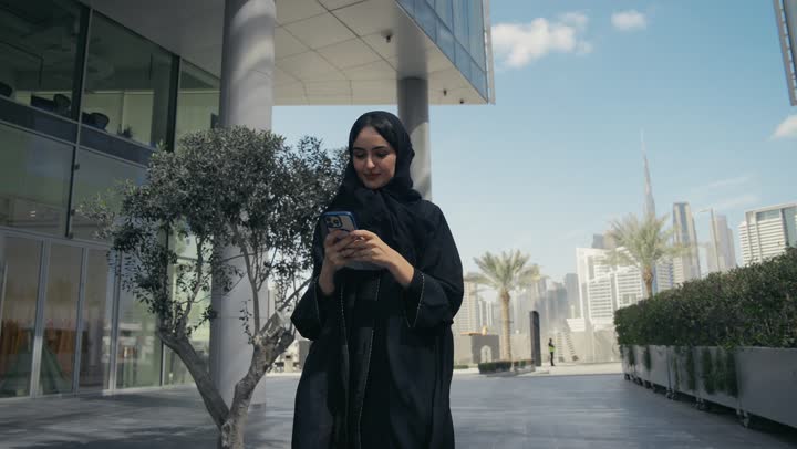 A Saudi Arabian Gulf woman using a mobile phone, gestures and facial expressions indicating happiness, exchanging news via text messages, chatting with family and friends, an Emirati woman messaging online, using modern technologies