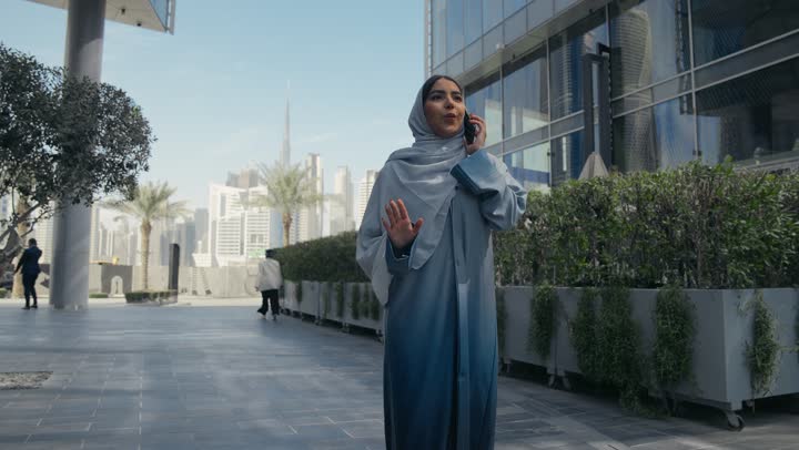 الانزعاج بسماع اخبار سيئه، تبادل الاخبار والأحاديث مع الاصدقاء والأهل، إمرأة عربية سعودية خليجية محجبة ترتدي العباءة تقوم بالتحدث عبر الهاتف المحمول، ايماءات السعادة و السرور بإجراء مكالمة هاتفية، سيده اماراتيه ترتدي عباءه ملونه تسيرفي مكان خارجي