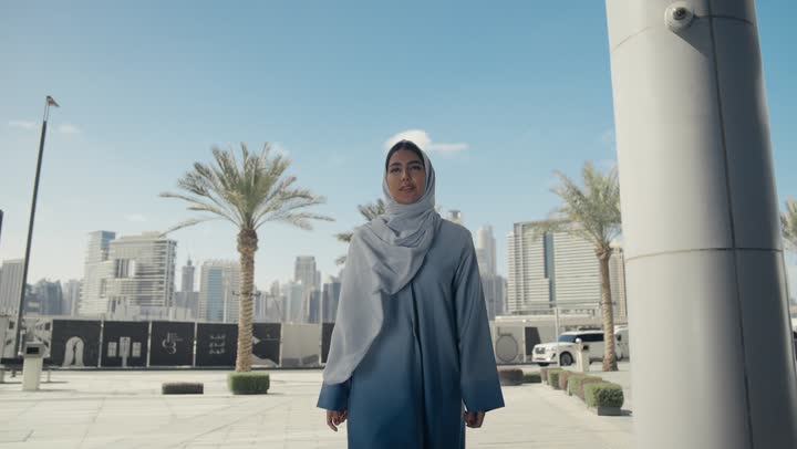 Caring about one's outward appearance, a smiling, veiled Emirati Gulf Arab woman wearing a gray abaya, walking upright and confidently, the concept of femininity and elegance, a Saudi woman walking confidently in the city center