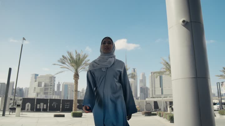 Caring about one's outward appearance, a smiling, veiled Emirati Gulf Arab woman wearing a gray abaya, walking upright and confidently, the concept of femininity and elegance, a Saudi woman walking confidently in the city center