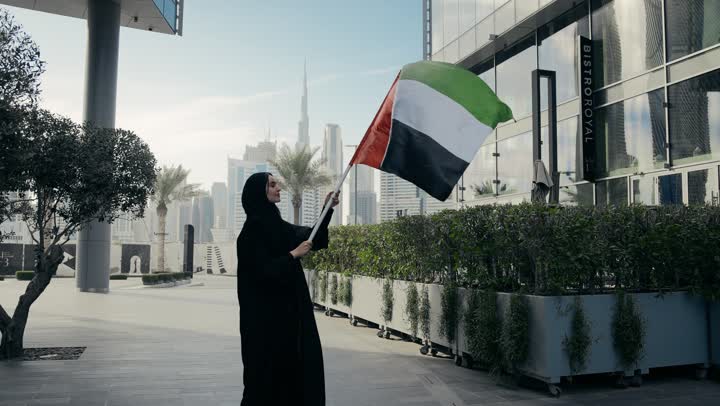 The concept of patriotism, participation in national holidays and occasions, pride, dignity and honor, UAE National Independence Day, an Emirati woman carrying the UAE flag and raising it high, UAE National Day, an Emirati woman wearing a black abaya celebrating the National Day