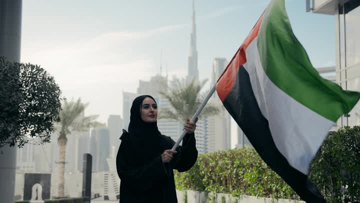 حب الوطن والانتماء اليه، العزه والشموخ والافتخار، يوم الاستقلال الوطني الاماراتي،  سيده اماراتيه تحمل علم دولة الامارات وتقوم برفعه الي الاعلي، ذكرى اليوم الوطني الاماراتي، امرأه اماراتية ترتدي عباءه سوداء تحتفل باليوم الوطني لدولة الامارات