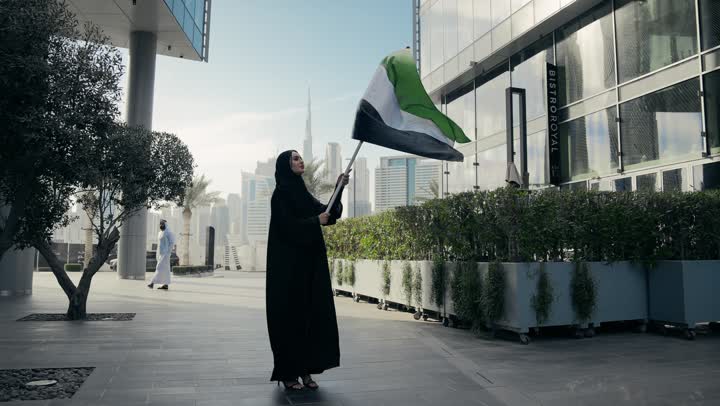 Love of the homeland and belonging to it, pride, dignity and honor, UAE National Independence Day, an Emirati woman carrying the UAE flag and raising it high, UAE National Day commemoration, an Emirati woman wearing a black abaya celebrating UAE National Day
