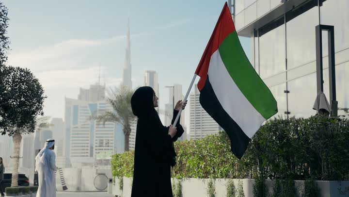 حب الوطن والانتماء اليه، العزه والشموخ والافتخار، يوم الاستقلال الوطني الاماراتي،  سيده اماراتيه تحمل علم دولة الامارات وتقوم برفعه الي الاعلي، ذكرى اليوم الوطني الاماراتي، امرأه اماراتية ترتدي عباءه سوداء تحتفل باليوم الوطني لدولة الامارات