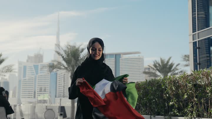 العزه والشموخ والافتخار، يوم الاستقلال الوطني الاماراتي،  سيده اماراتيه تحمل علم دولة الامارات وتقوم بتقبيله، ذكرى اليوم الوطني الاماراتي، امرأه اماراتية ترتدي عباءه سوداء تحتفل باليوم الوطني لدولة الامارات العربية المتحدة