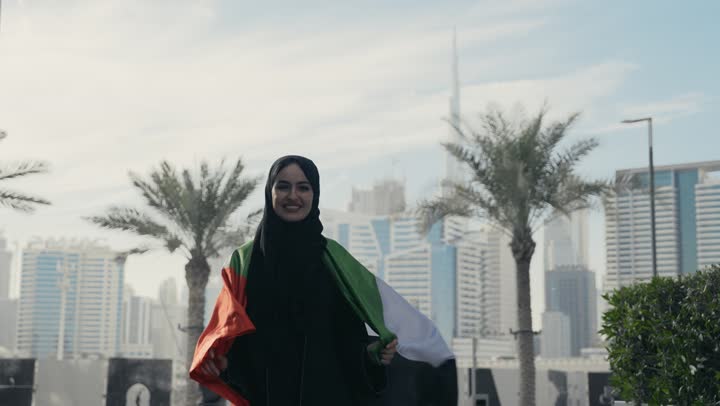 ايماءات وجه تدل علي الشموخ والافتخار، يوم الاستقلال الوطني الاماراتي،  سيده اماراتيه تحمل علم دولة الامارات علي ظهرها، ذكرى اليوم الوطني الاماراتي، امرأه اماراتية ترتدي عباءه سوداء تحتفل باليوم الوطني لدولة الامارات العربية المتحدة