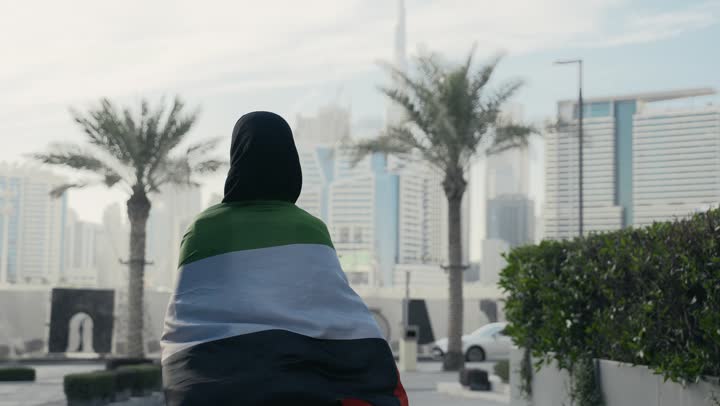 UAE National Independence Day, Emirati woman holding the UAE flag on her back, facial expressions indicating pride and dignity, UAE National Day commemoration, Emirati woman wearing a black abaya celebrating UAE National Day