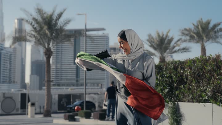 Emirati woman wearing a gray abaya celebrating UAE National Day, Emirati woman holding the UAE flag and kissing it, facial expressions indicating love and happiness, UAE National Day, UAE National Independence Day