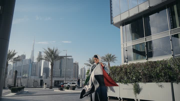 امرأه اماراتية ترتدي عباءه رماديه تحتفل باليوم الوطني لدولة الامارات العربية المتحدة، سيده اماراتيه تحمل بيدها علم دولة الامارات وتقوم بتقبيله، ايماءات وجه تدل علي الحب و السعادة،  ذكرى اليوم الوطني الاماراتي، يوم الاستقلال الوطني الاماراتي