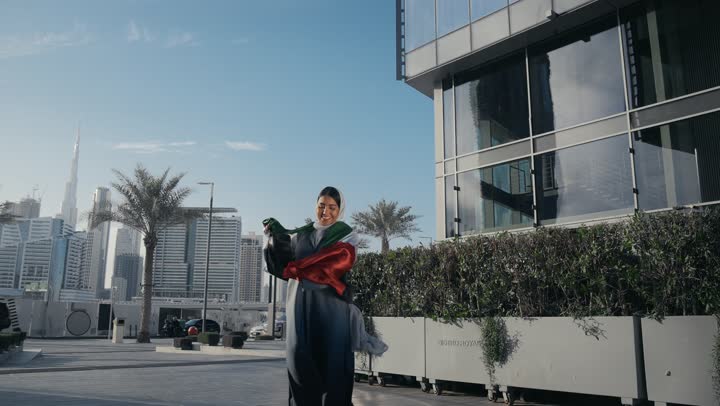 Pride and appreciation for the country's achievements, the identity of the 51st UAE National Day, celebrating the UAE National Day, UAE Independence Day, love and belonging to the homeland, an Arab Gulf Emirati woman hugging the UAE flag, gestures of love and pride
