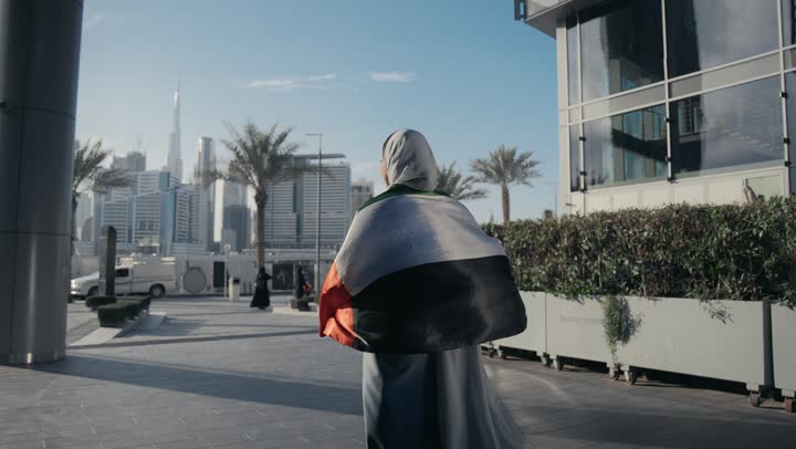 الاعتزاز والفخر بإنجازات البلاد، هوية اليوم الوطني الاماراتي 51، الإحتفال باليوم الوطني الإماراتي، يوم استقلال الإمارات، الحب والانتماء للوطن، امرأه عربيه خليجيه اماراتيه تحمل علم الامارات علي ظهرها تسير في الهواء الطلق