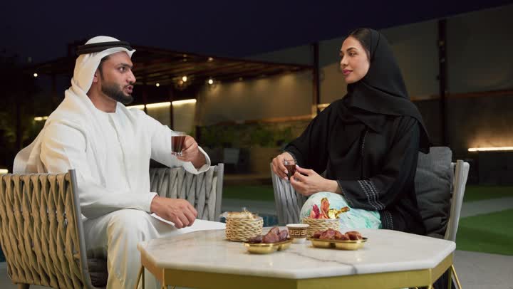 شرب القهوة العربية، قضاء أوقات عائلية ممتعة, التفاهم والترابط الفكري بين الزوجين، تناول الوجبات الخفيفة والتسالي، الجلوس في إحدى الشاليهات الاماراتية الراقية، رجل عربي خليجي اماراتي يرتدي الكندورة والغترة يقوم بتبادل الأحاديث مع زوجته في الهواء الطلق