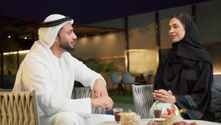 شرب القهوة العربية، قضاء أوقات عائلية ممتعة, التفاهم والترابط الفكري بين الزوجين، تناول الوجبات الخفيفة والتسالي، الجلوس في إحدى الشاليهات الاماراتية الراقية، رجل عربي خليجي اماراتي يرتدي الكندورة والغترة يقوم بتبادل الأحاديث مع زوجته في الهواء الطلق