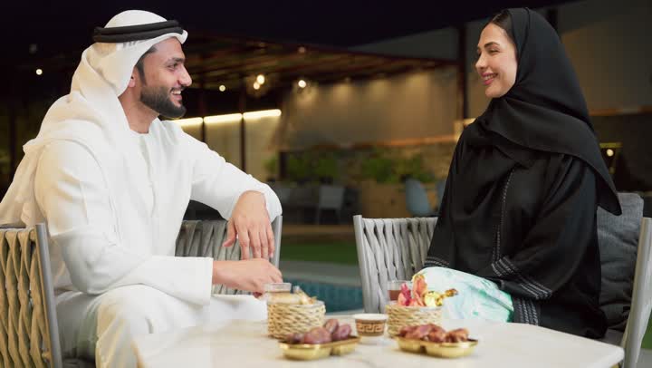 شرب القهوة العربية، قضاء أوقات عائلية ممتعة, التفاهم والترابط الفكري بين الزوجين، تناول الوجبات الخفيفة والتسالي، الجلوس في إحدى الشاليهات الاماراتية الراقية، رجل عربي خليجي اماراتي يرتدي الكندورة والغترة يقوم بتبادل الأحاديث مع زوجته في الهواء الطلق