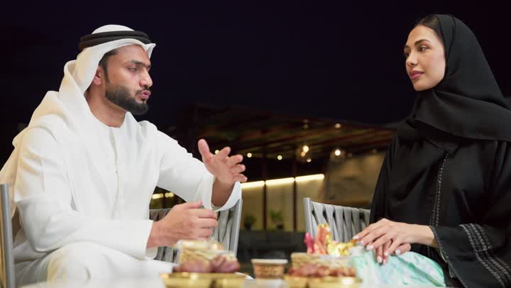 شرب القهوة العربية، قضاء أوقات عائلية ممتعة, التفاهم والترابط الفكري بين الزوجين، تناول الوجبات الخفيفة والتسالي، الجلوس في إحدى الشاليهات الاماراتية الراقية، رجل عربي خليجي اماراتي يرتدي الكندورة والغترة يقوم بتبادل الأحاديث مع زوجته في الهواء الطلق