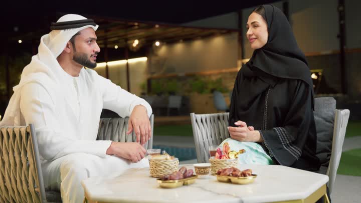 شرب القهوة العربية، قضاء أوقات عائلية ممتعة, التفاهم والترابط الفكري بين الزوجين، تناول الوجبات الخفيفة والتسالي، الجلوس في إحدى الشاليهات الاماراتية الراقية، رجل عربي خليجي اماراتي يرتدي الكندورة والغترة يقوم بتبادل الأحاديث مع زوجته في الهواء الطلق