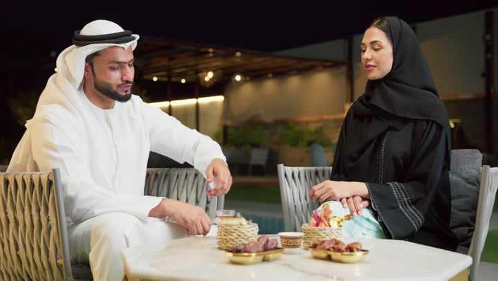 الجلوس في إحدى الشاليهات الاماراتية الراقية، شرب القهوة العربية، قضاء أوقات عائلية ممتعة, التفاهم والترابط الفكري بين الزوجين، تناول الوجبات الخفيفة والتسالي، زوجان عربيان خليجيان اماراتيان يجلسان في الهواء الطلق ويقومان بتبادل الأحاديث