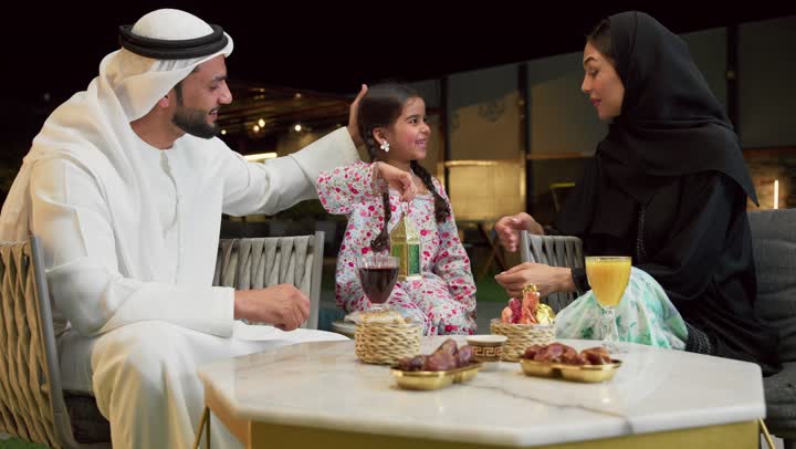 قضاء وقت ممتع في جلسة خارجية عائلية في احدى الشاليهات، زينة واكسسوار الأعياد والمناسبات الاسلامية، فتاة عربية خليجية اماراتية تحمل بيدها فانوس معدني مزخرف مضيء بجانب والديها، ضيافة شهر رمضان المبارك، أجواء ليلية رمضانية روحانية