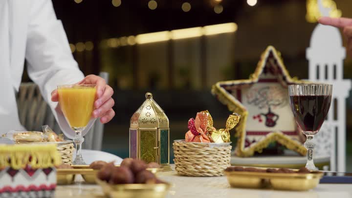 طاولة مليئة بالزينة والديكورات الرمضانية، حسن الاستقبال وكرم الضيافة في شهر رمضان المبارك، صديقان عربيان خليجيان اماراتيان يرتديان الكندورة والغترة يجلسان في شاليه سياحي يقومان بتبادل الاحاديث بتعابير السرور، الاستمتاع بتناول المشروبات الباردة