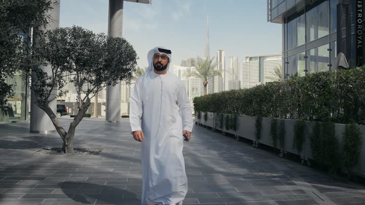 Walking around public areas, enjoying the fresh air, taking a walk in the open air, an Emirati Gulf Arab man wearing a kandura and ghutra having a good time in a park in the Emirates, a walk in nature