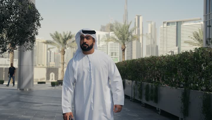 Outdoors, walking around and enjoying the fresh air, an Emirati Gulf Arab man wearing a kandura and ghutra having a good time in a park in the Emirates, a nature walk, walking around public areas,