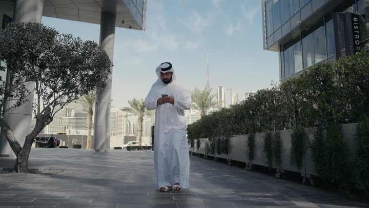 Chatting and communicating with family, hearing news and happy surprises, taking a walk in the open air, making a phone call on a mobile phone, an Emirati Gulf Arab man having a good time in a park in the Emirates, a tour in nature
