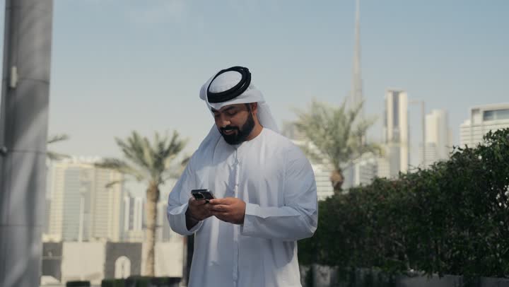 Outdoor walk, chatting and communicating with family, hearing news and happy surprises, making a phone call via mobile phone, an Arab Gulf Emirati man having a good time in a park in the Emirates, a tour in nature