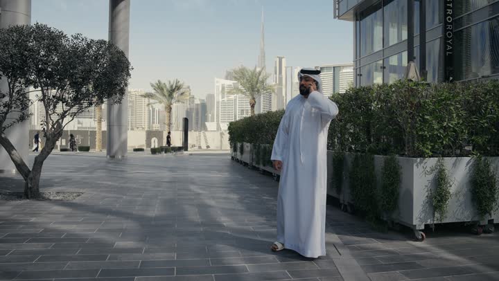 A walk in nature, a walk in the open air, chatting and communicating with family, hearing news and happy surprises, making a phone call via mobile phone, an Arab Gulf Emirati man having a good time in a park in the Emirates