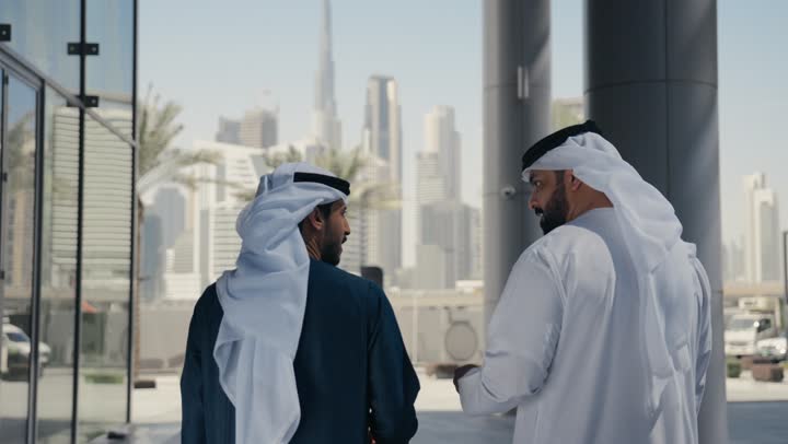 مفهوم الأناقة والاهتمام بالمظهر الخارجي ،الاستمتاع والتجول مع الاصدقاء ، قضاء اوقات ممتعه ، المشي فى الخارج ، استنشاق الهواء النقي في وقت النهار، صديقان عربيان خليجيان اماراتيان يرتديان الكندوره والغتره ، النظر الى بعضهما بتعابير السرور.