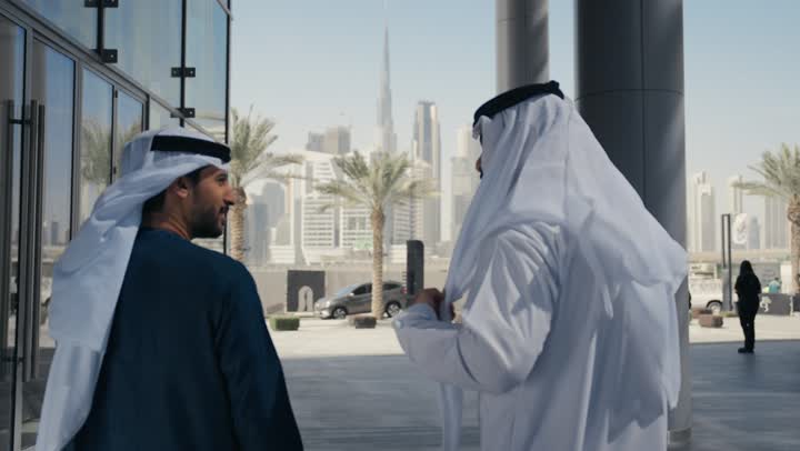 قضاء اوقات ممتعه مع الاصدقاء ، مفهوم الأناقة والاهتمام بالمظهر الخارجي ، المشي فى الخارج ،الاستمتاع والتجول واستنشاق الهواء النقي في وقت النهار، صديقان عربيان خليجيان اماراتيان يرتديان الكندوره والغتره ، النظر الى بعضهما بتعابير السرور.