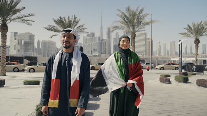 Learning about the culture and history of the Emirati people, love of the homeland and belonging to it, celebrating National Day on December 2, UAE Independence Day, a photo of a couple wearing Emirati dress and placing the UAE flag on their shoulders