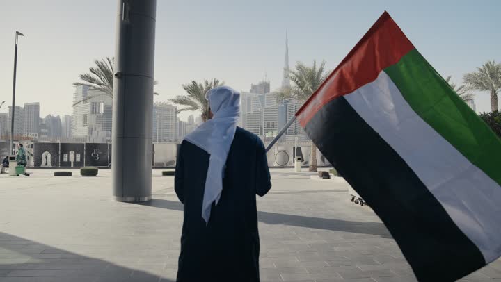 تصوير لرجل يرتدي الكندوره والغتره يرفع علم دولة الامارات العربية المتحدة ، ايماءات الفخر والسعاده ، إحياء ذكرى استقلال البلاد، يوم استقلال الإمارات ، التعرف على ثقافات وتاريخ شعب الامارات، حب الوطن والانتماء إليه, الاحتفال باليوم الوطني 2 ديسمبر