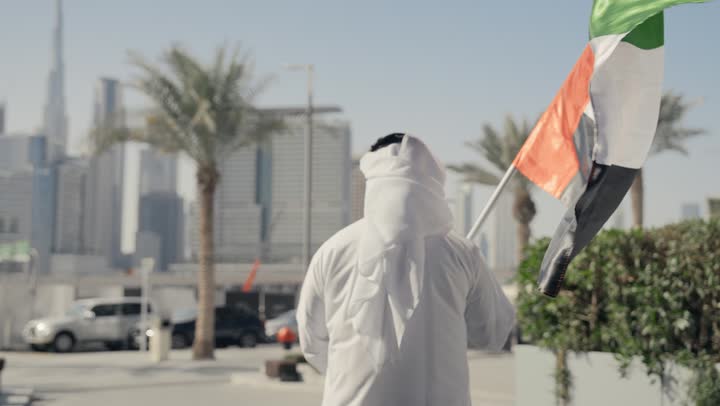 Gestures of pride and happiness, the anniversary of the founding of the Union 1971, learning about the cultures and history of the people of the Emirates, reviving the love of the homeland and belonging to it, a picture of a man wearing a kandura and ghutra raising the flag of the United Arab Emirates, UAE Independence Day, celebrating the National Day, December 2