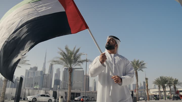 حب الوطن والانتماء إليه ،تصوير لرجل يرتدي الكندوره والغتره يرفع علم دولة الامارات العربية المتحدة ، يوم استقلال الإمارات ، الاحتفال باليوم الوطني 2 ديسمبر، ايماءات الفخر والسعاده ، ذكرى تأسيس الاتحاد1971، التعرف على ثقافات وتاريخ شعب الامارات